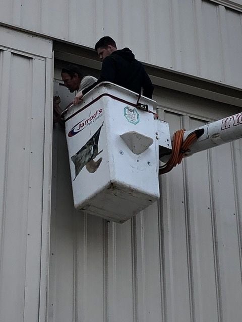 2 of Jarrod's Pest Control bird techs sealing up cracks between a hangar door and buidling